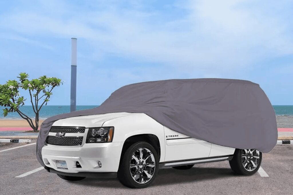 White SUV partially covered with a gray car cover under a blue sky.
