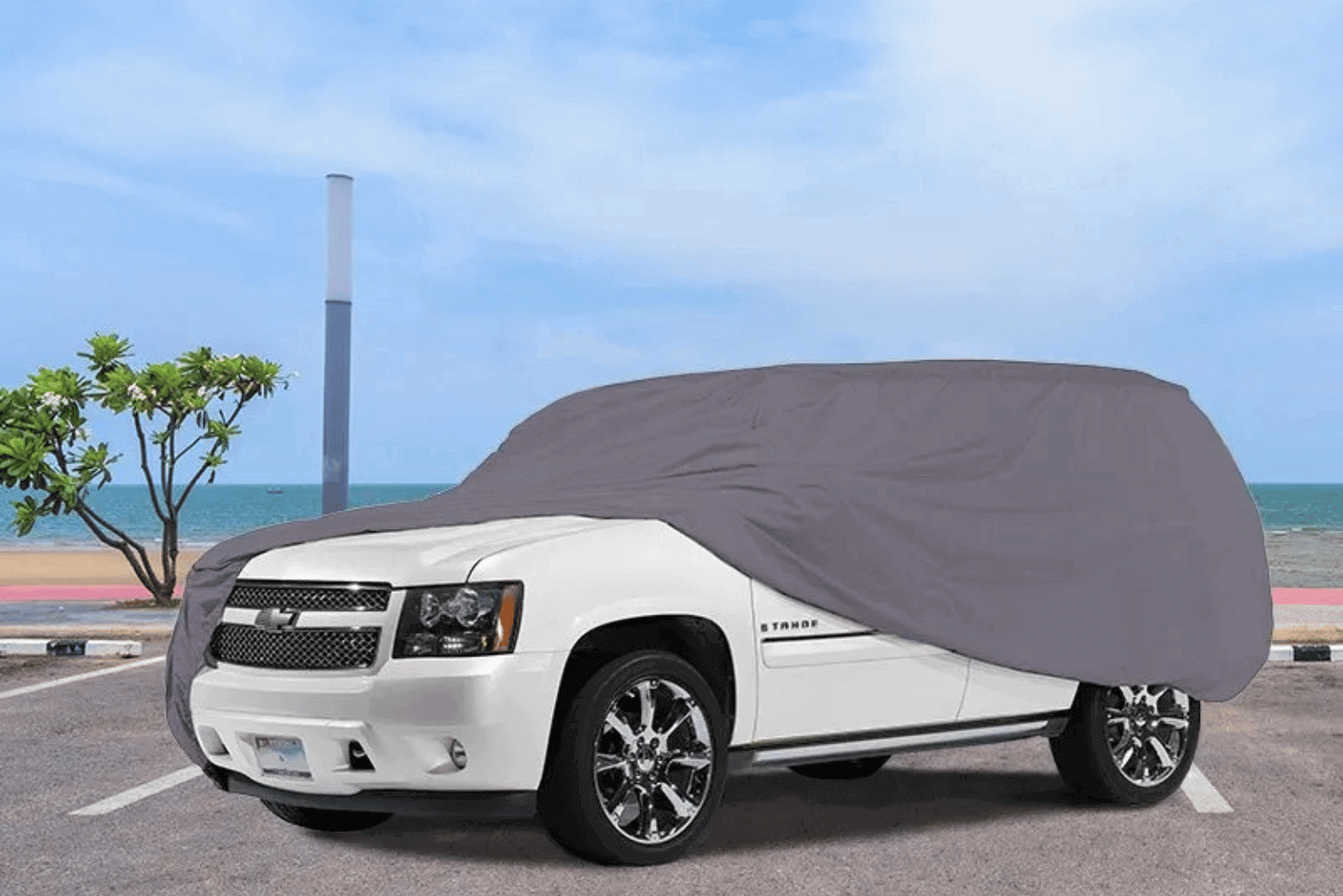White SUV partially covered with a gray car cover under a blue sky.