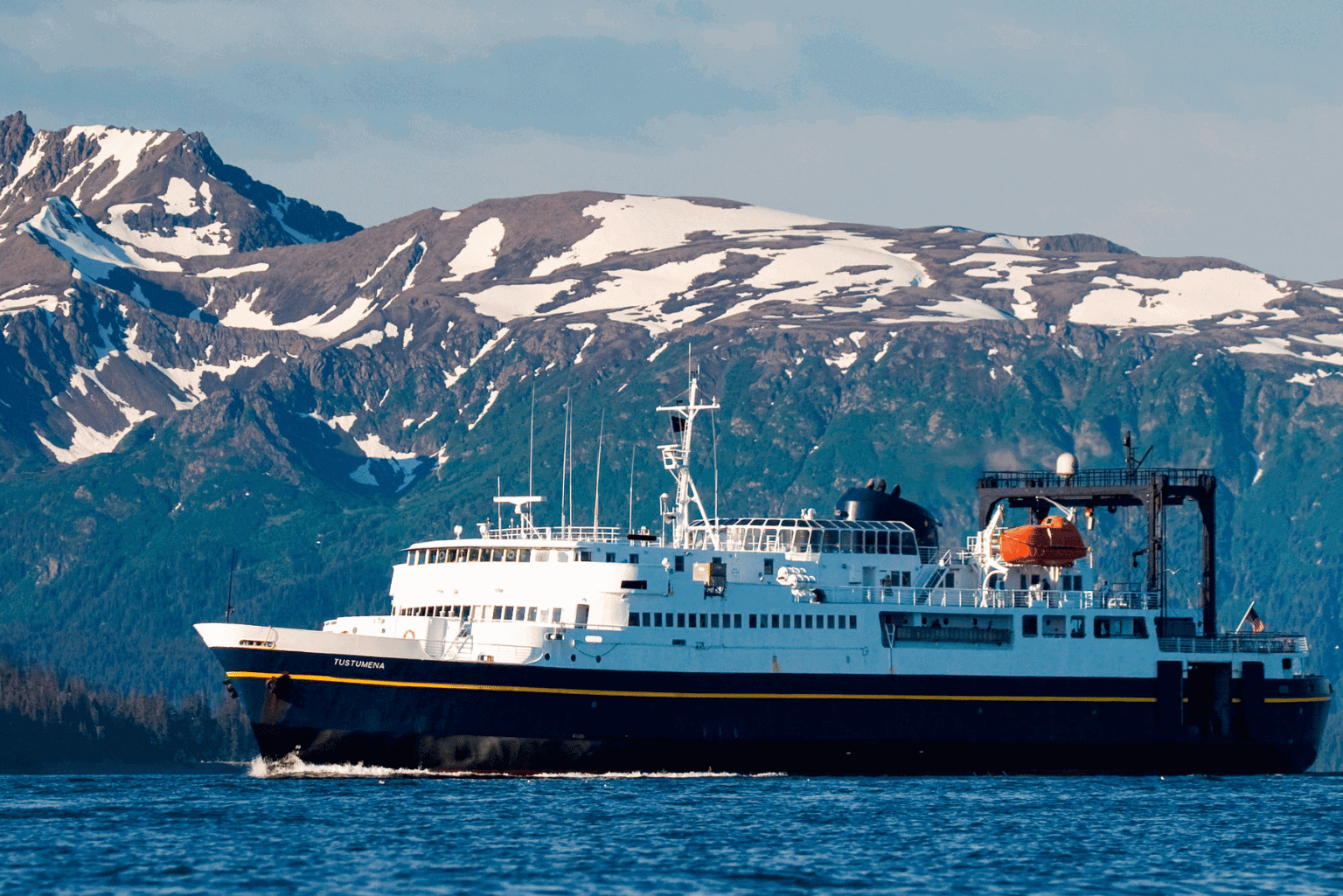 A large ferry boat sailing near snowy mountains.