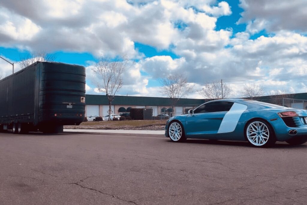 A blue sports car parked on a paved area under a partly cloudy sky.