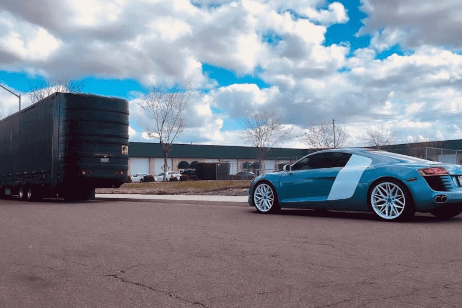 A blue sports car parked on a paved area under a partly cloudy sky.
