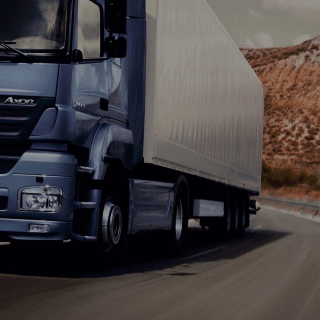 A blue semi-truck driving on a highway through a mountainous area.