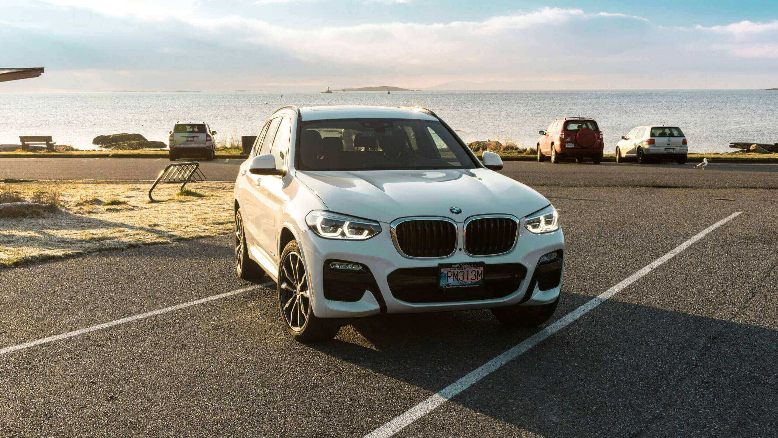 A white BMW SUV parked in a lot near the beach at sunset.